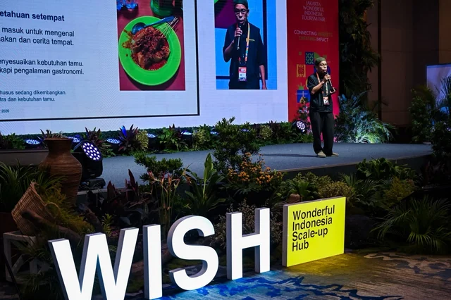 Pak Indra standing on stage during his presentation, with illuminated WISH letters at the front of the stage.