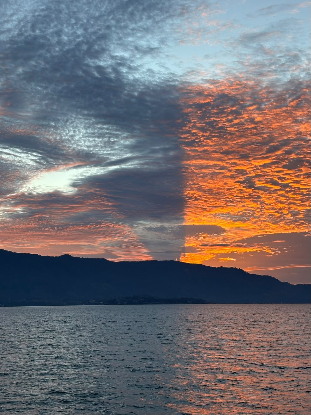An orange sky by the lake. Warm cloud colours above rippling water and a silhouette of hills.