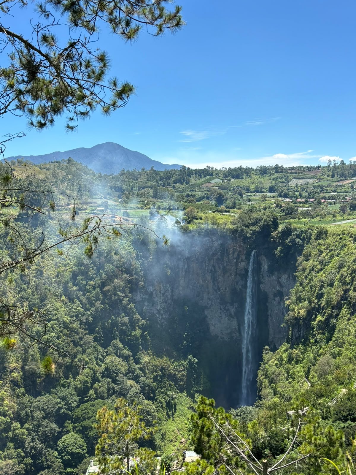 Sipiso-Piso from the valley rim. A slender waterfall framed by cliffs and the green highlands.